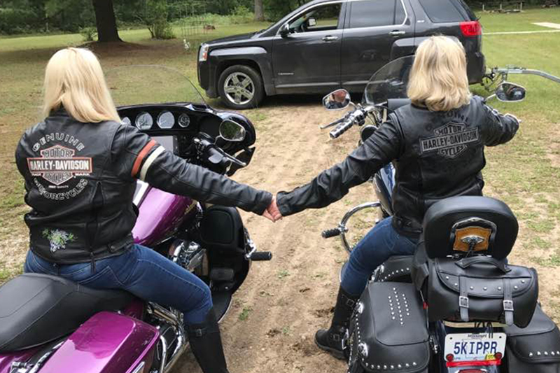 Tammy Smith and Julie Ferris sit on their Harley motorcycles, while holding hands.