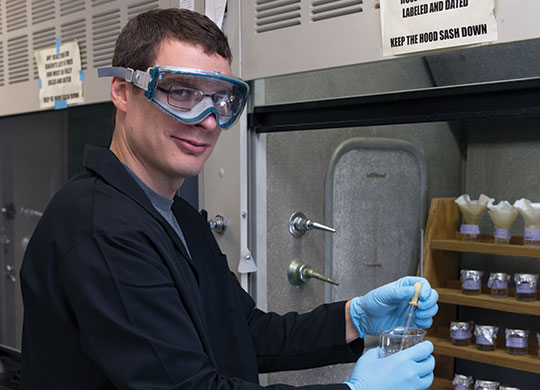 2017 Student Research Fellowship student participant Ian Steinke posing in a chemistry lab while wearing safety glasses.